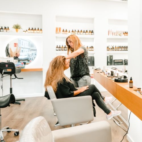 Foto de Silvia realizando un corte de cabello femenino en peluquería atravit en ciutadella de Menorca. Vemos a la clienta con una preciosa melena rubia frente espejo. 